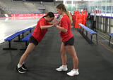 Athlete performing a standing partner push-up exercise in an ice hockey arena