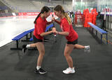 Athletes performing a single-leg partner stick wrestle exercise in an ice hockey arena