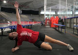 Athlete performing a knee-supported side plank with torso rotation exercise in an ice hockey arena