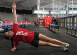 Athlete performing a side plank with torso rotation with feet stacked in an ice hockey arena