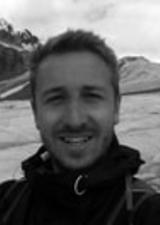 A young man with a crew cut and backpack stands in front of a glacier