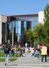 Front facade of the MacKimmie Student Centre with rainbow painted stairs and many students going to and fro