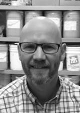 Bald man with beard and glasses in front of shelf full of 5 gallon sample pails