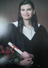 young woman with long dark hair holding a diploma and bouquet with graduation robes on