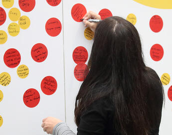 Woman interacting with an activation station, placing a coloured sticky note on a board.