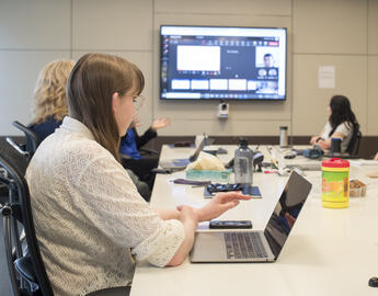 A young woman on a laptop in a board meeting room.