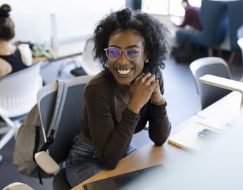 A young Black woman sitting at a desk and smiling.