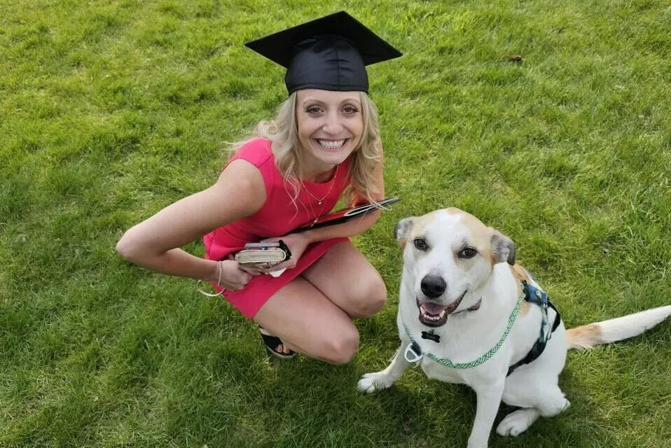 A person in a grad cap smiles with her dog