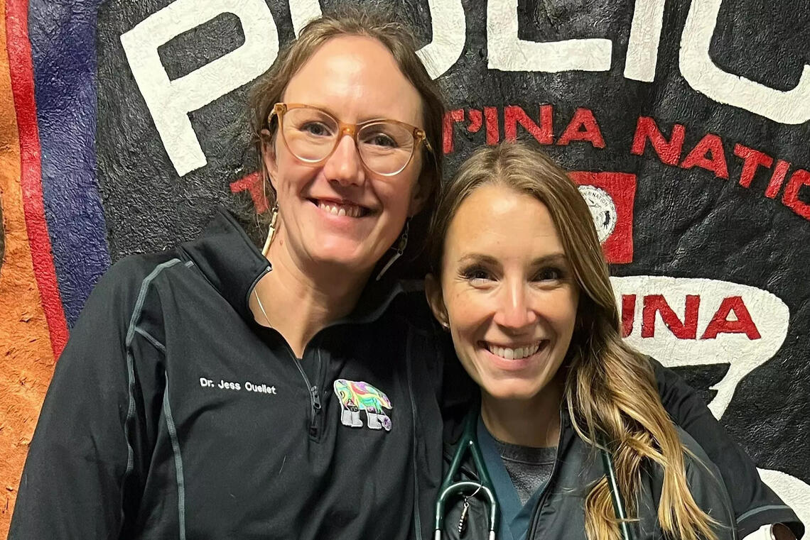 Two veterinarians stand side by side smiling at the camera