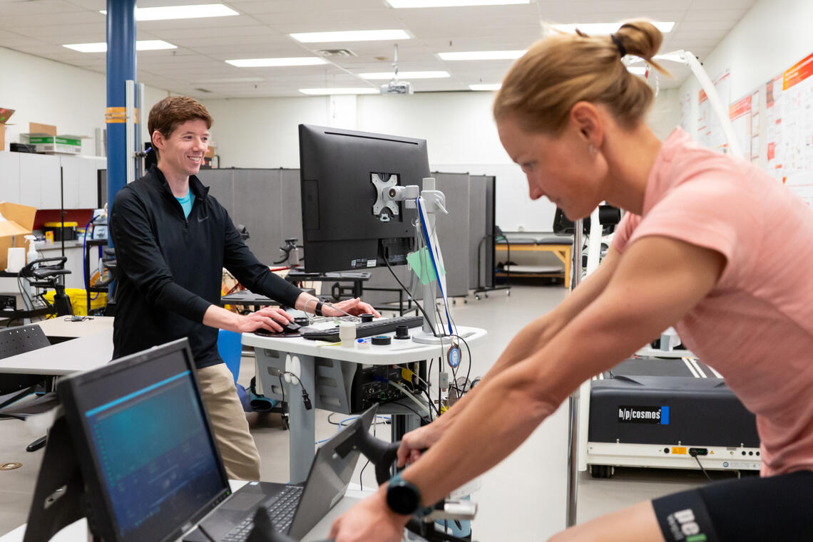 A man on a computer monitors a woman riding an exercise bike