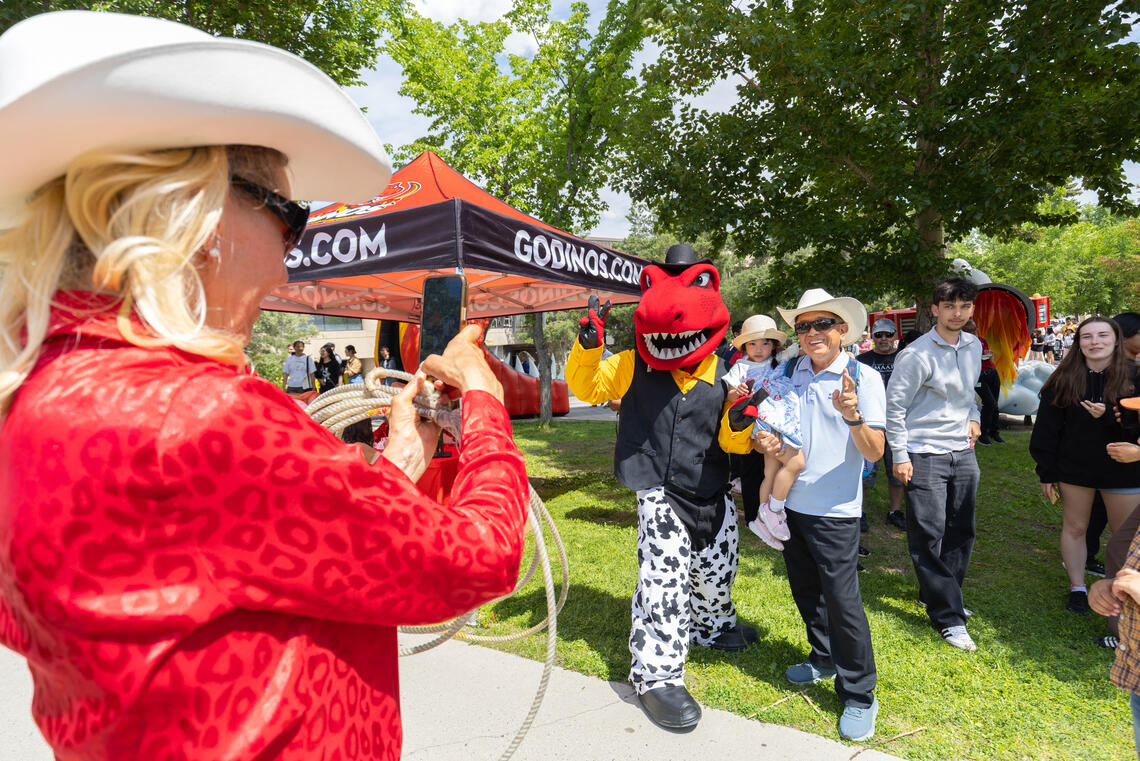 A person in western wear poses with a red dinosaur mascot