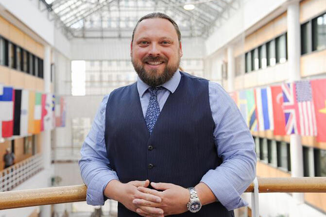 A man in a tie and suit vest smiles at the camera